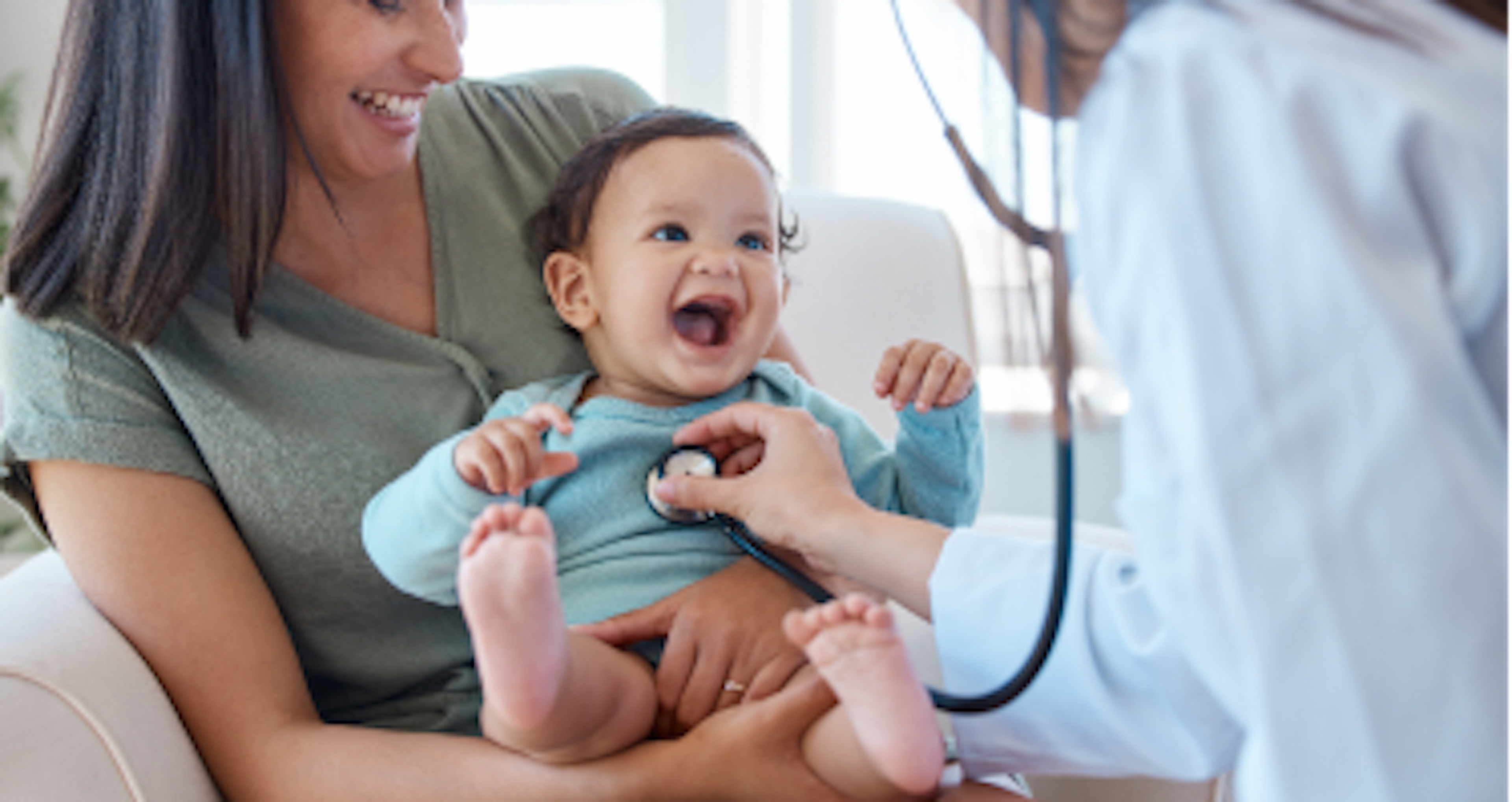 A healthcare professional using a stethoscope on a young child who is sitting on an adult’s lap. The child’s face is obscured for privacy.