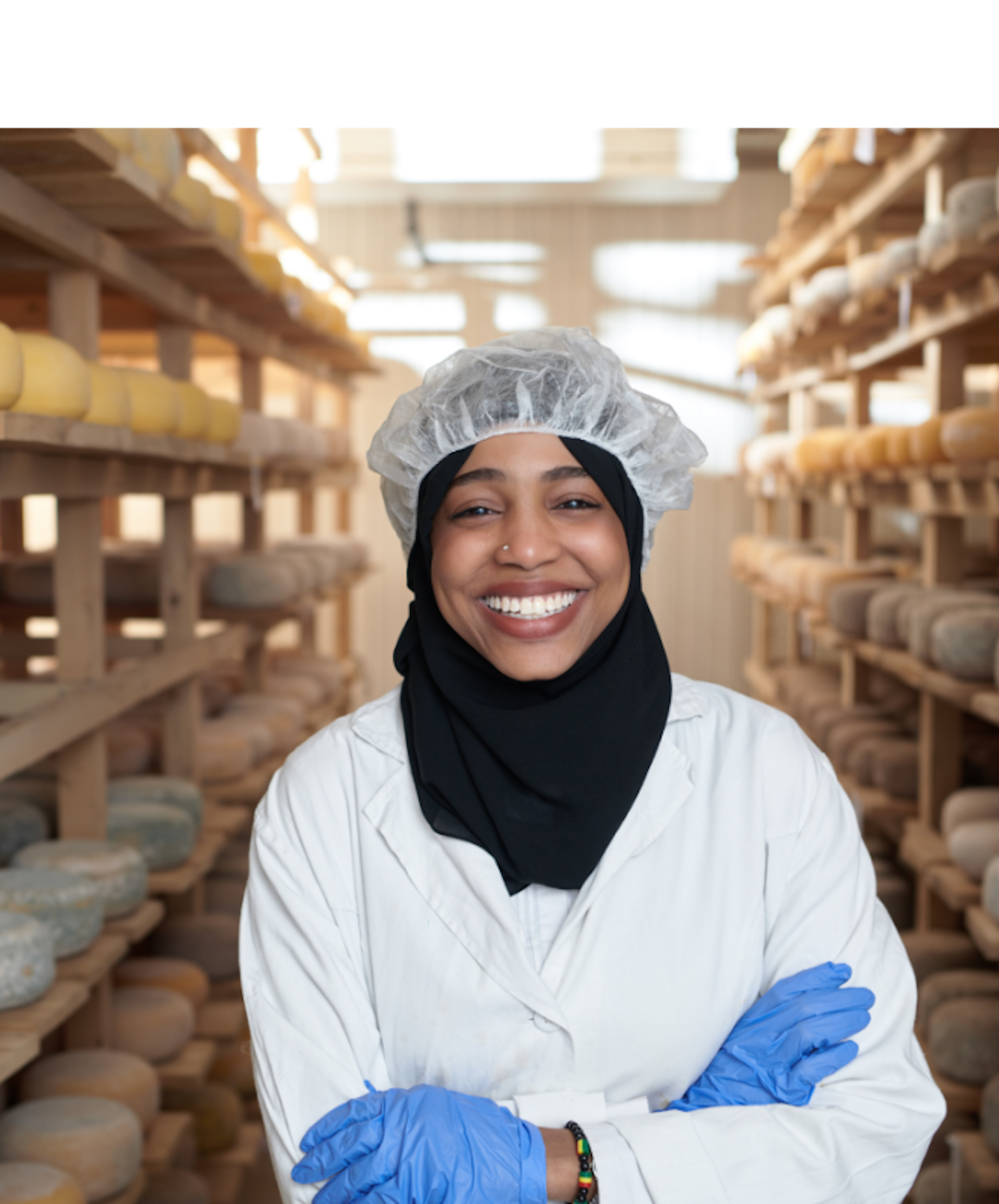 A person standing in a cheese aging room with shelves of cheese wheels