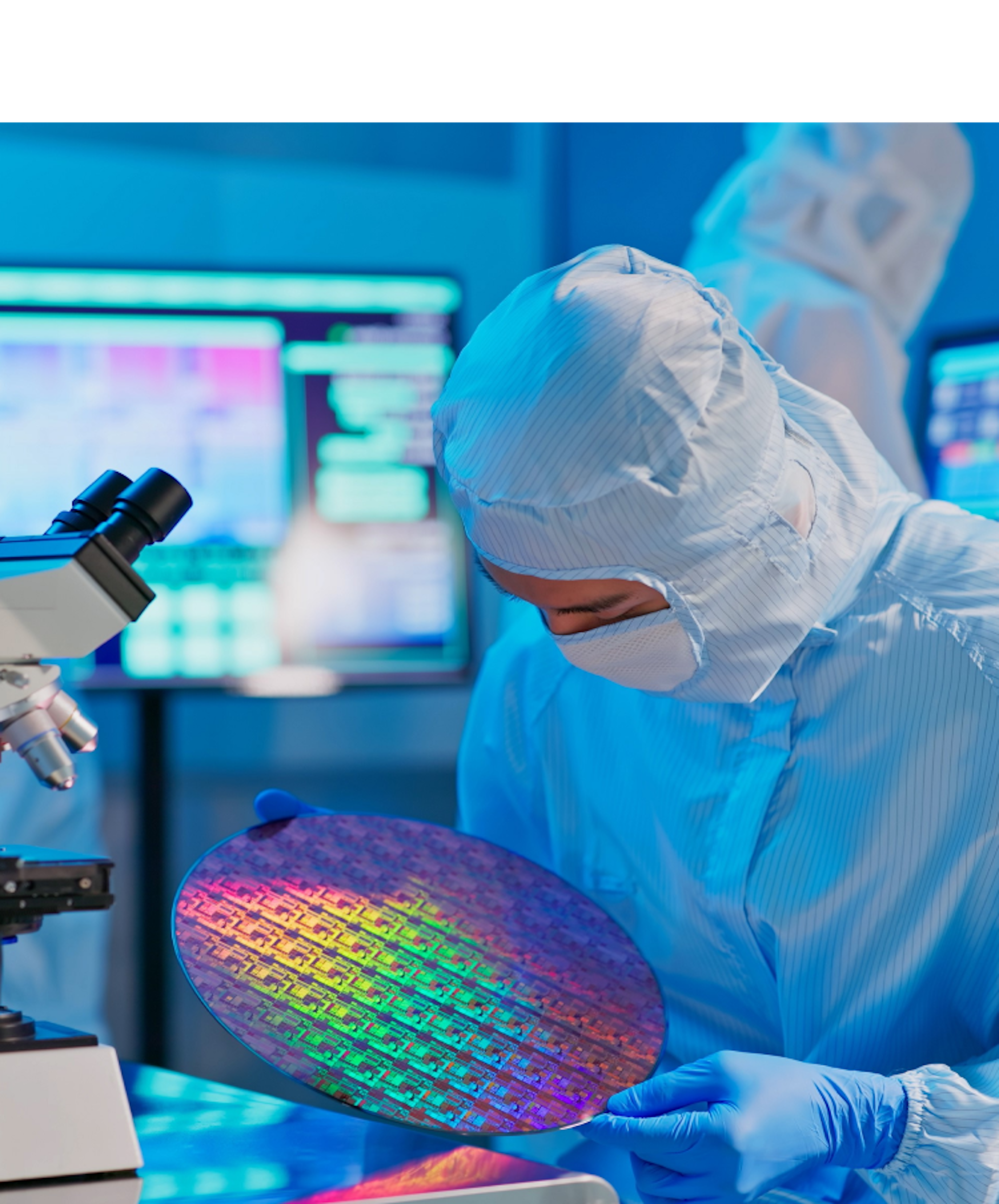 A person in a cleanroom suit examining a colorful silicon wafer under a microscope in a high-tech laboratory environment, indicating semiconductor manufacturing or research.