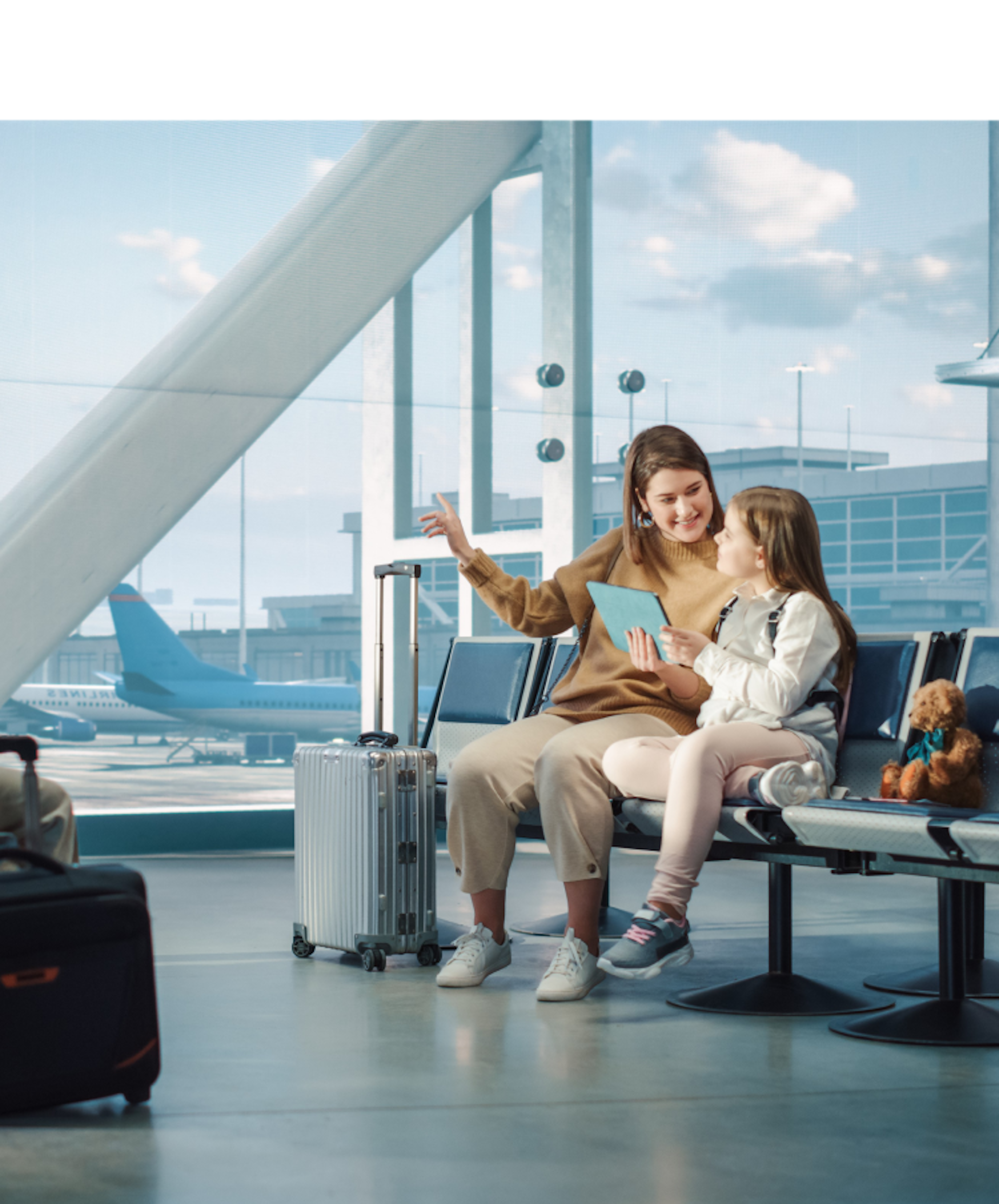 People sitting on airport in waiting area with airplanes in the background