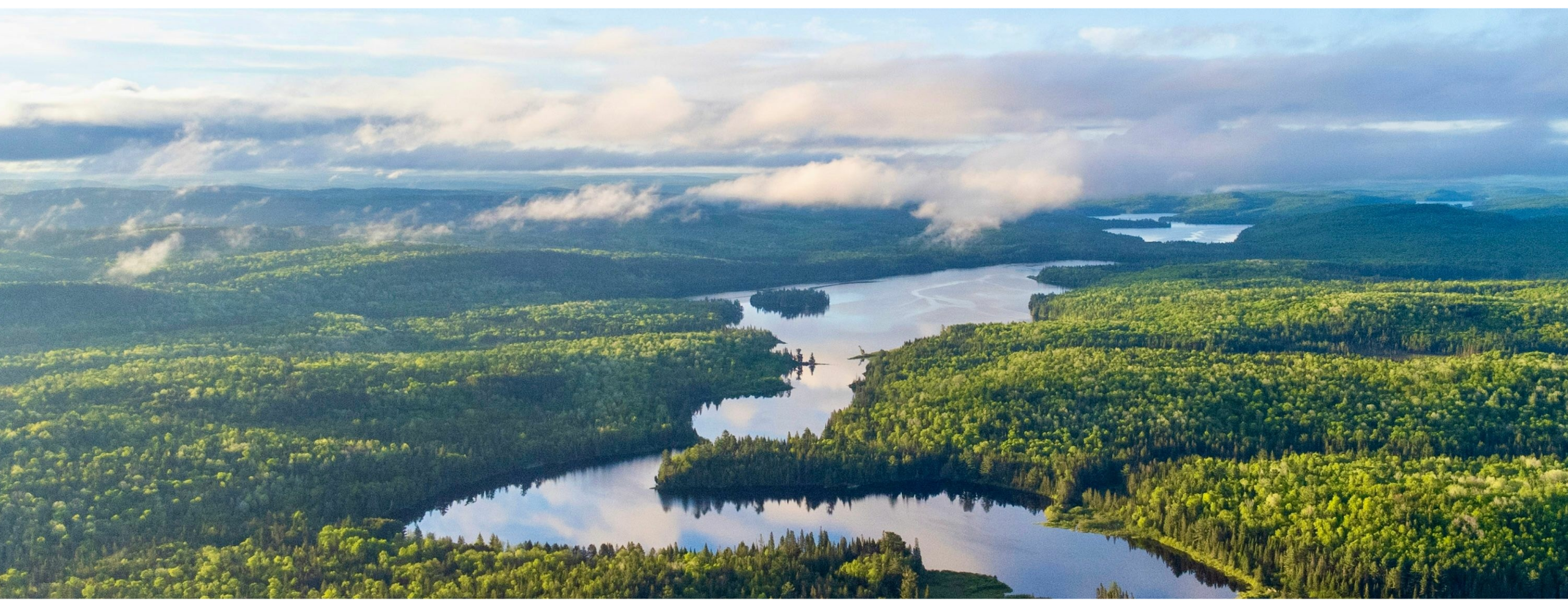 Aerial view of a vast forest landscape with interconnected lakes, partially covered by clouds on a sunny day.