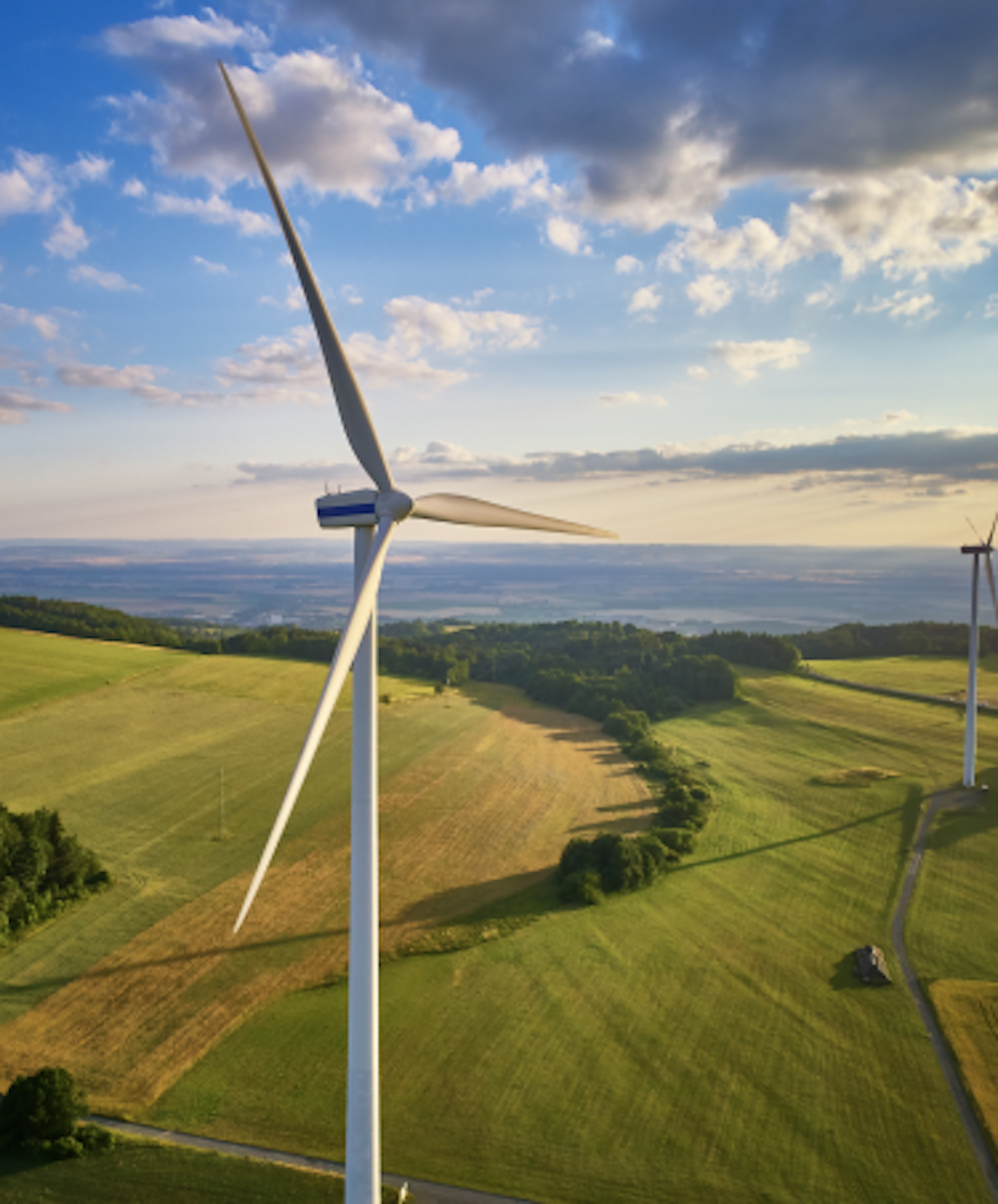 A scenic landscape with three large wind turbines on rolling green hills under a partly cloudy sky.