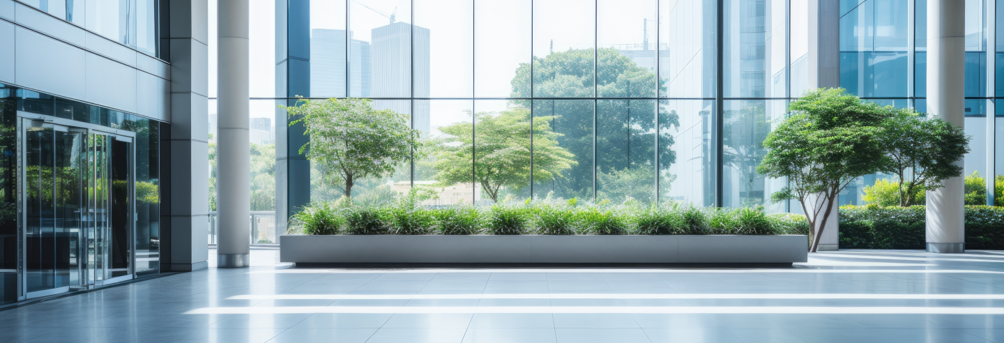 A modern building interior with large glass windows, trees, and plants.